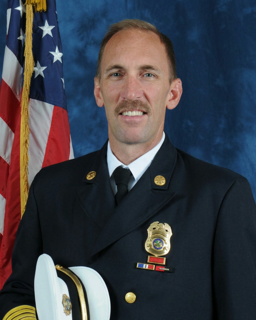 Official portrait of Art Andres in fire department dress uniform beside an American flag
